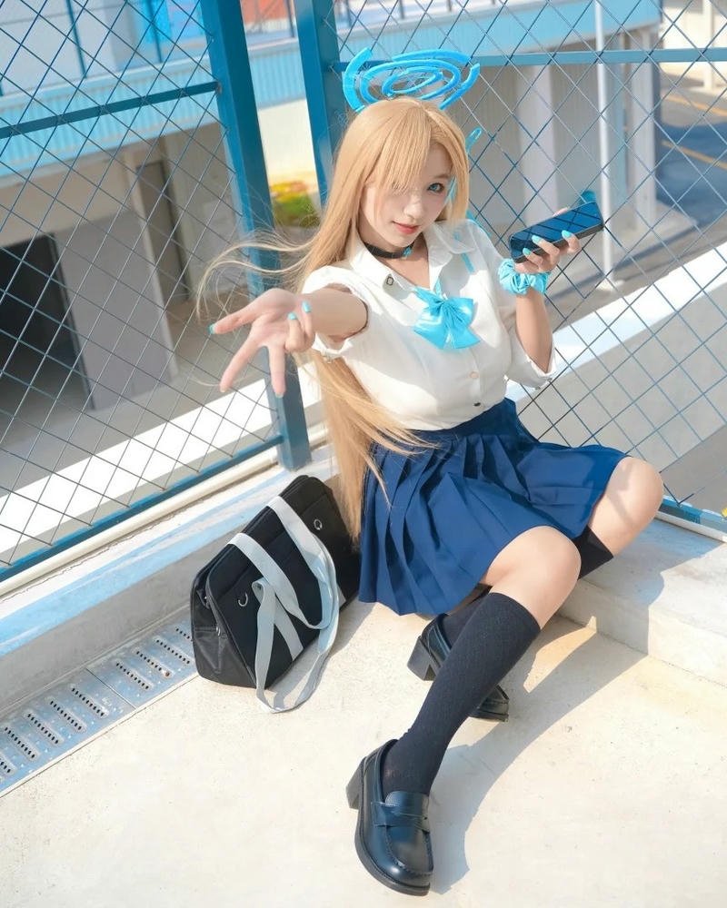 Cosplay học sinh tóc vàng váy xanh ngồi trên ghế đá